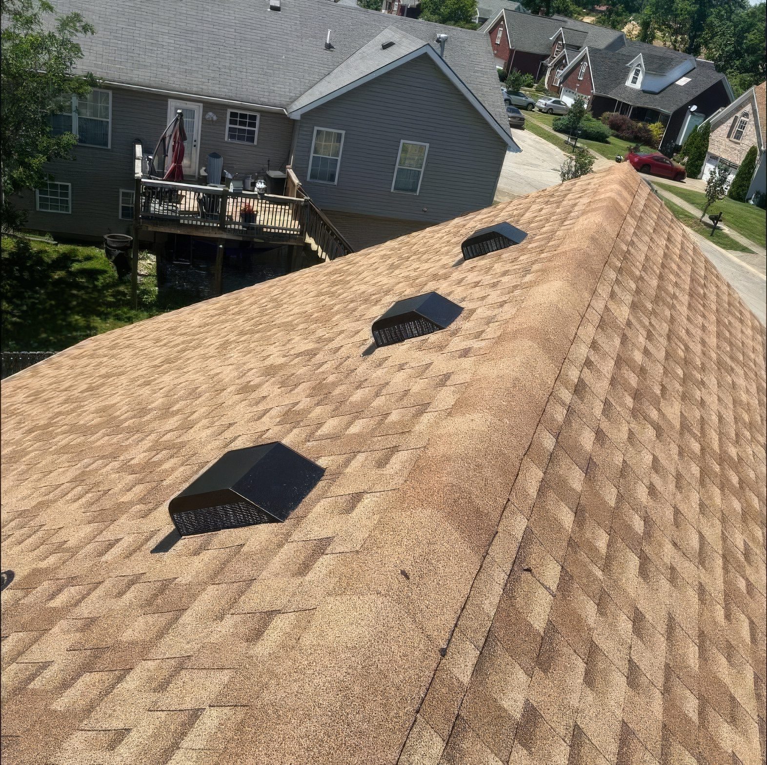 Down the ridge of a finished roof, three new vents in line, the neighborhood behind