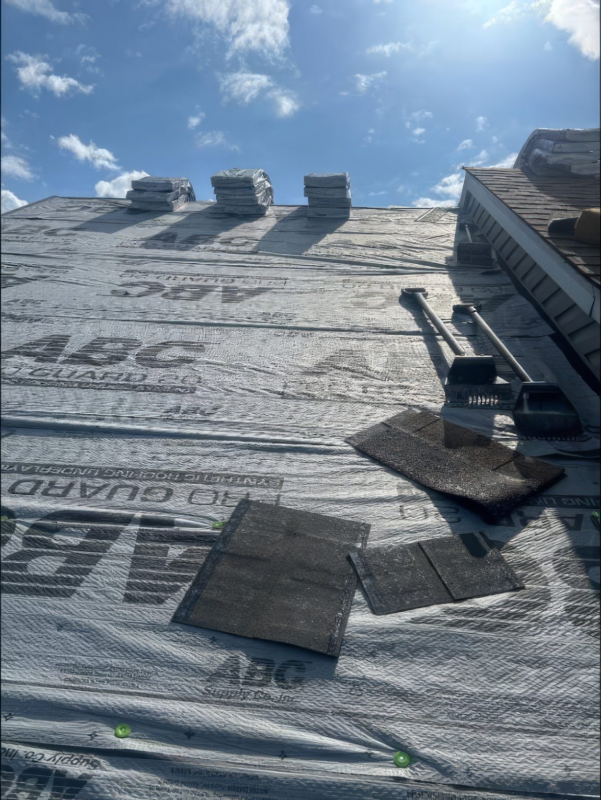Dried in: new synthetic underlayment across the whole roof, shingle bundles staged along the ridge